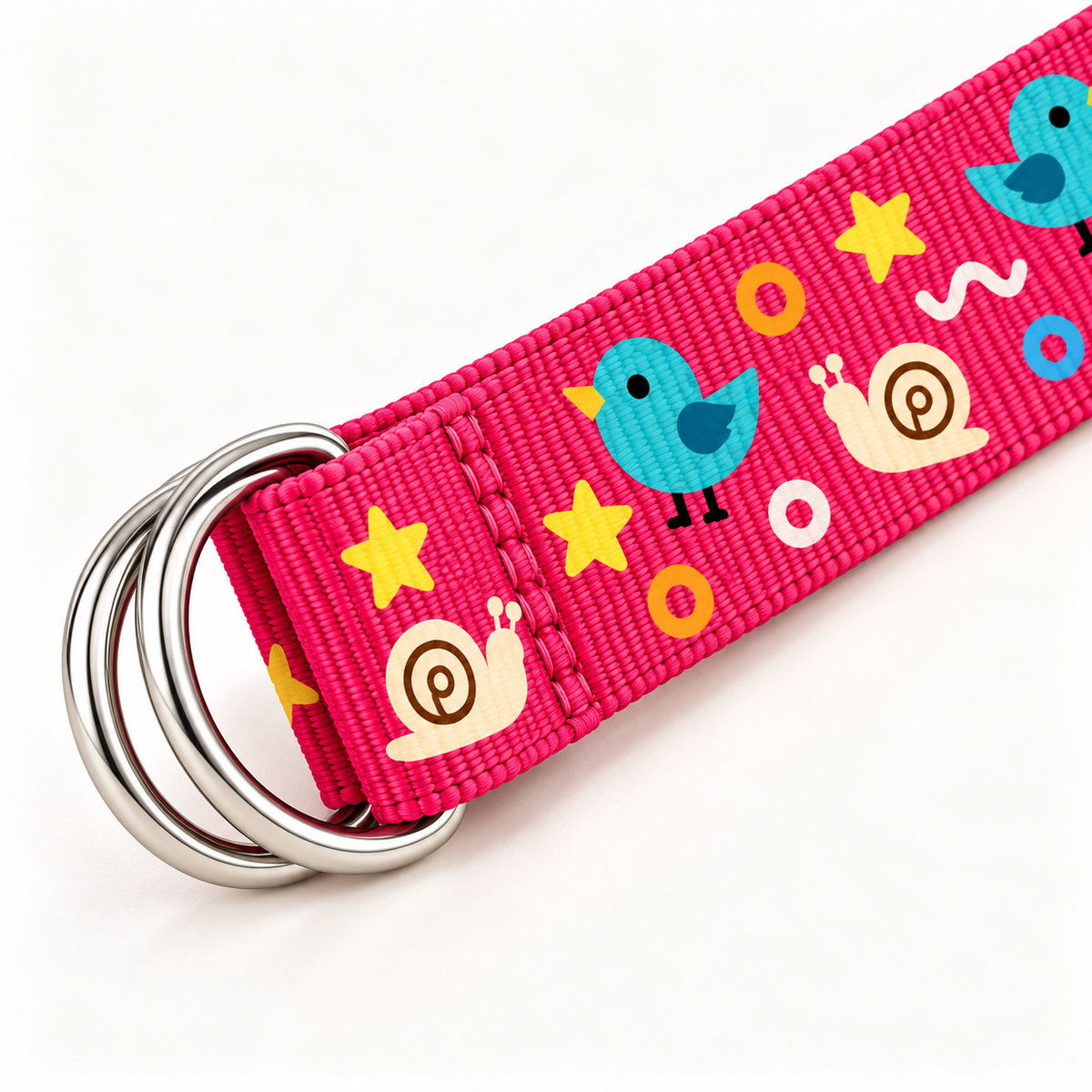 Close-up of a pink nylon webbing belt showing its paired silver-tone D-rings, stitched buckle attachment, woven texture and original bird, snail and shapes print on a warm-white background.