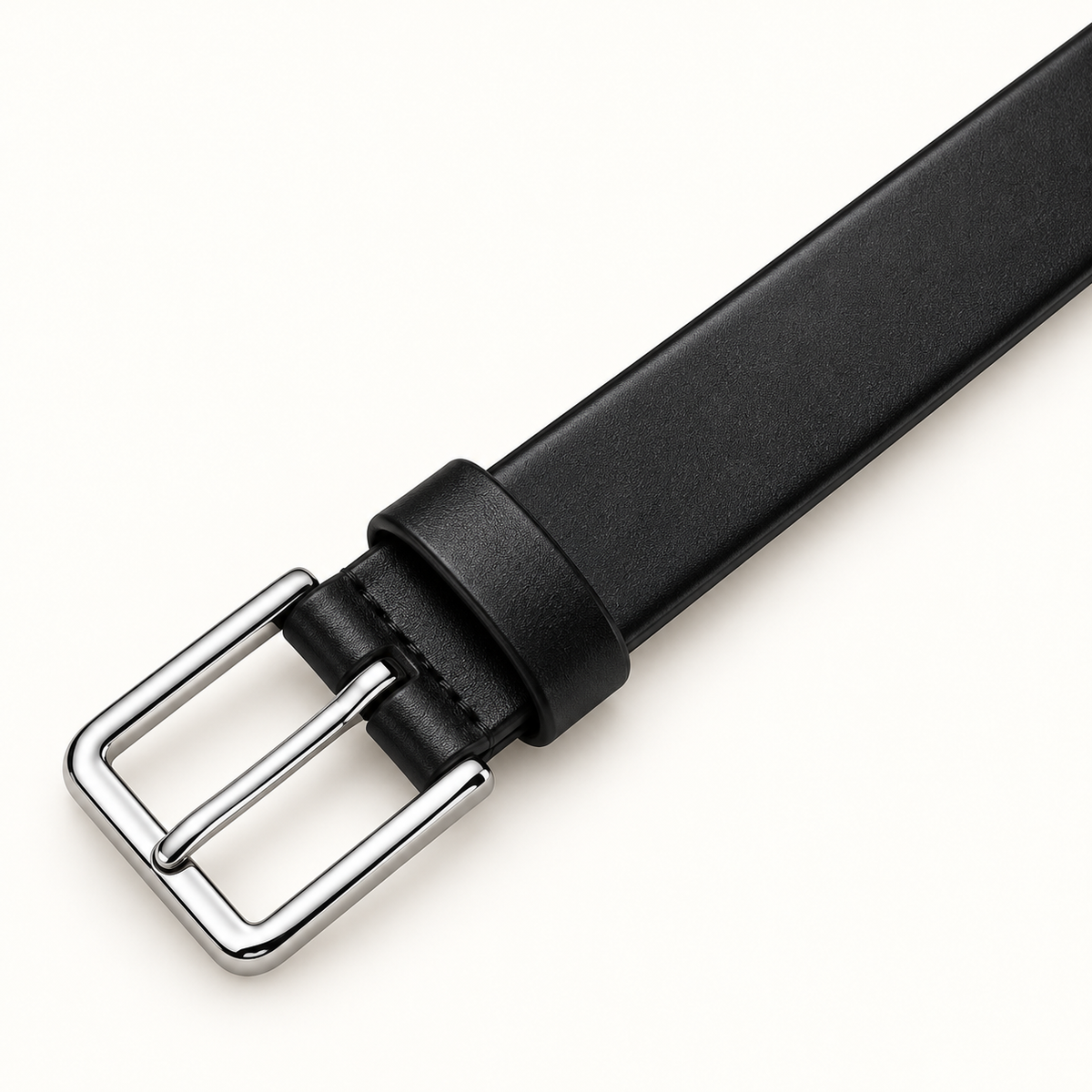 Close-up of the plain rectangular silver-tone pin buckle and matching black keeper on a slim smooth black leather belt against a warm-white background.