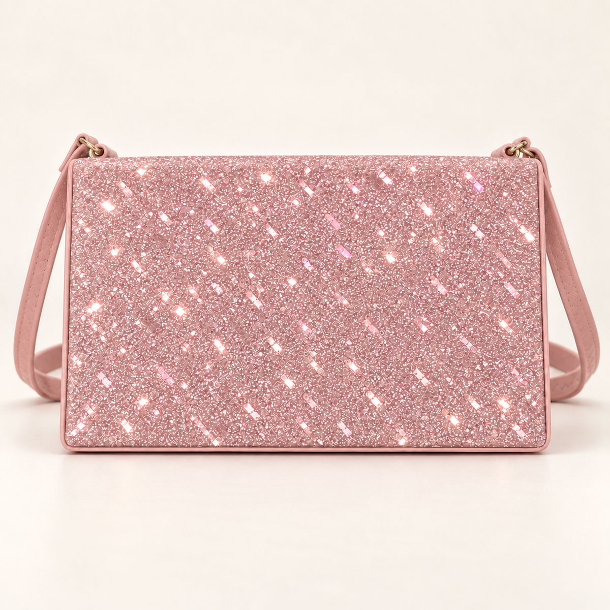 Front view of a blush pink rectangular women's sling bag with a sparkling glitter panel, matching shoulder strap and gold-tone strap rings on a plain light background