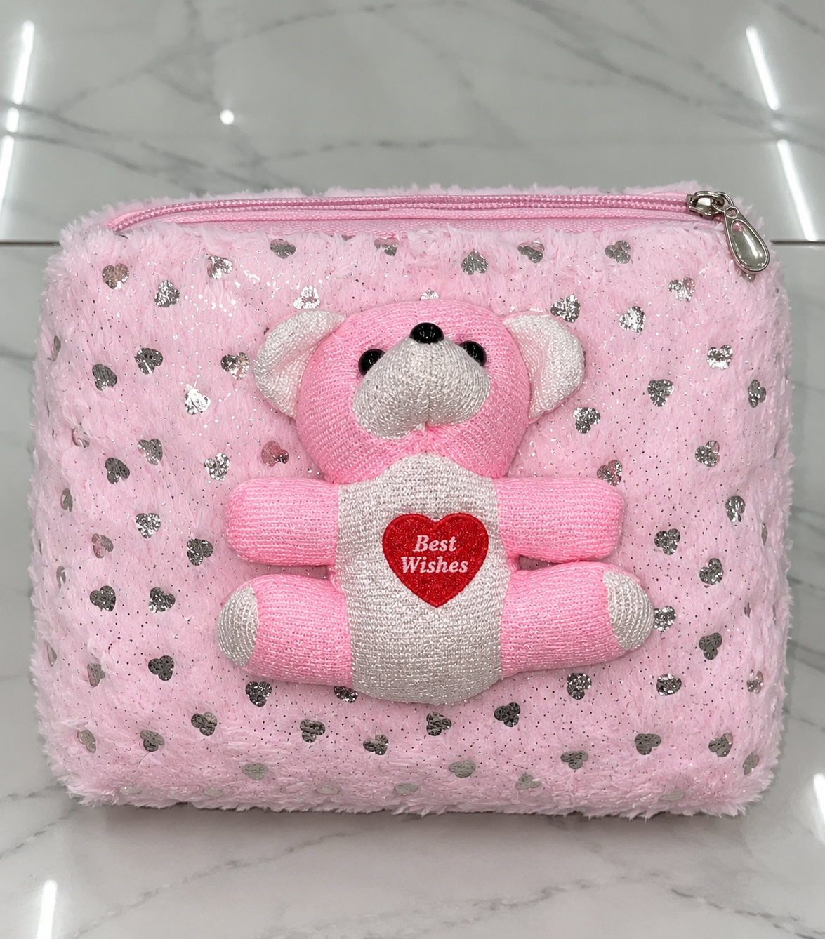 Pink fuzzy zip pouch photographed from the front, featuring silver heart motifs, a pink and white teddy bear with a red heart and silver-tone zip pull.